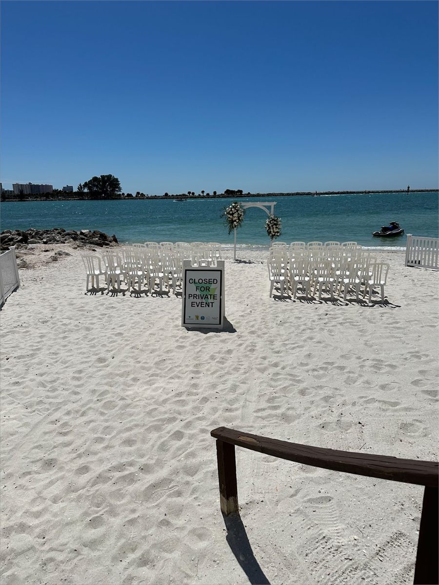 Beach ceremony set up on the sand with rows of white chairs and a floral arch