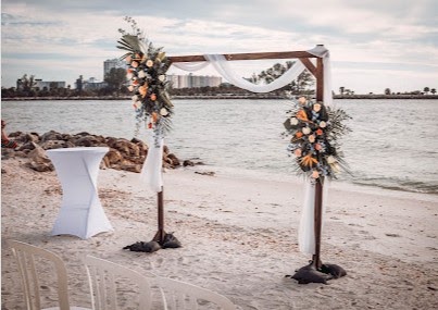 Wooden beach arbor with white draping and peach and blue floral arrangements
