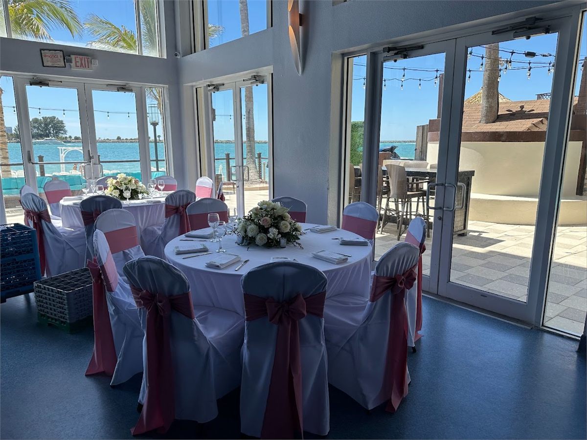Waterfront reception room with round tables, burgundy chair sashes and a white centerpiece