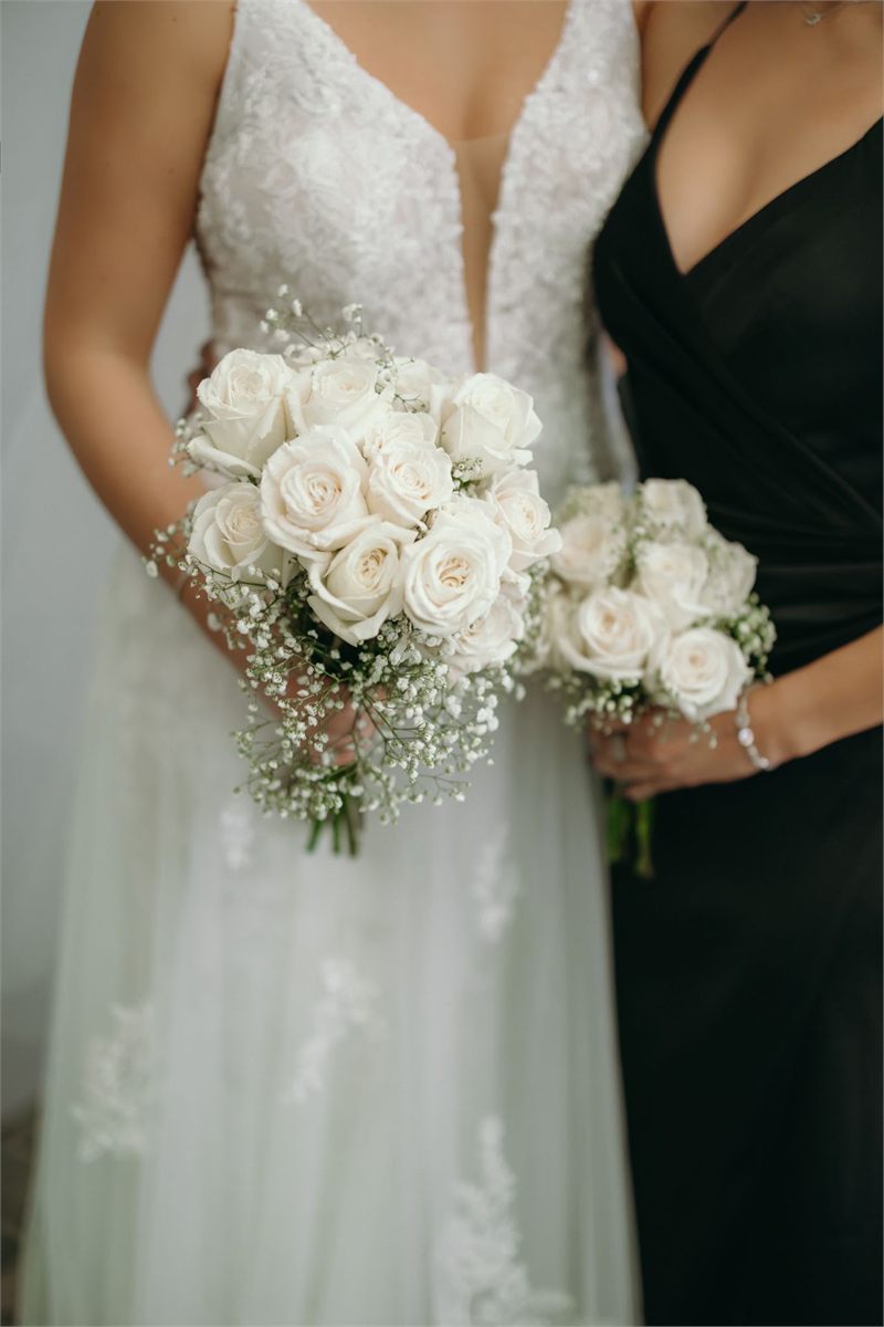 Bride and bridesmaid holding bouquets of white roses and baby's breath
