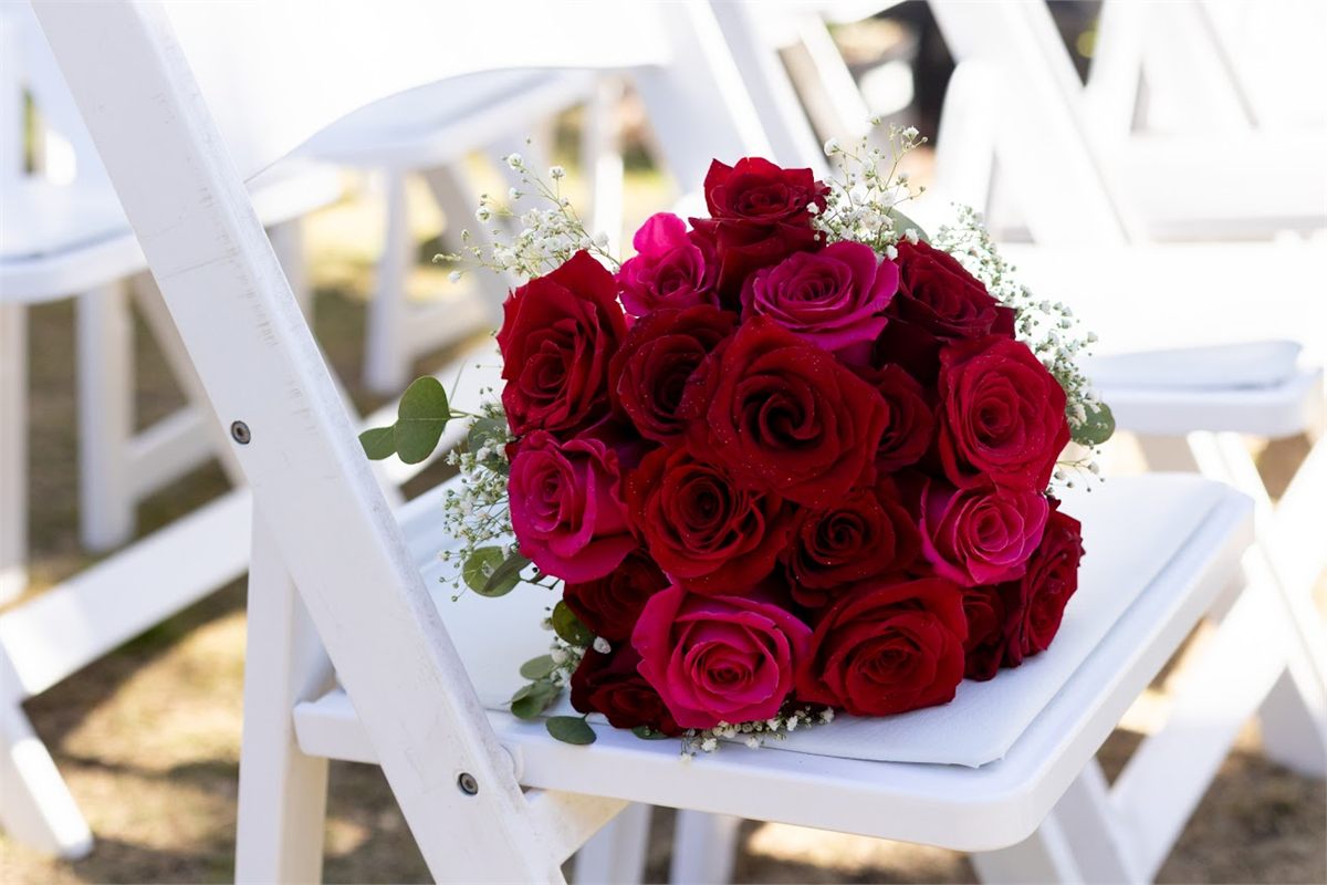 Bouquet of red and pink roses resting on a white folding chair at an outdoor ceremony