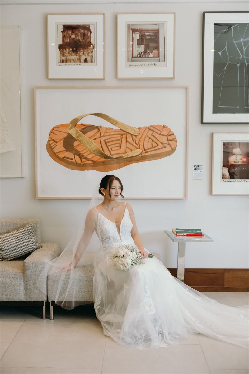 Bride seated in a lace gown holding a small white bouquet