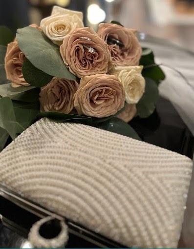 Bouquet of dusty rose and cream garden roses with eucalyptus, beside a white clutch