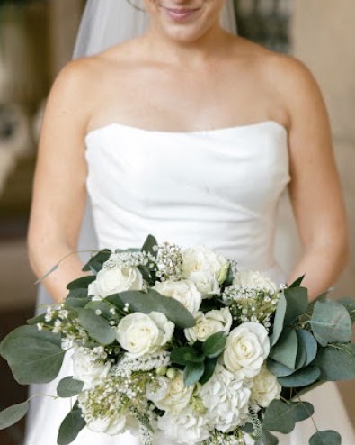 Bride in a strapless gown holding a bouquet of white roses and eucalyptus