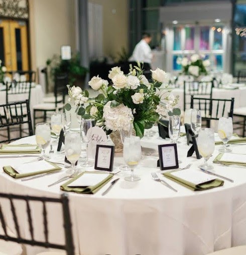 Round reception table with white roses, black picture frames and dark wood chairs