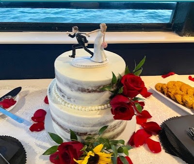 Two-tier wedding cake decorated with red roses and scattered rose petals