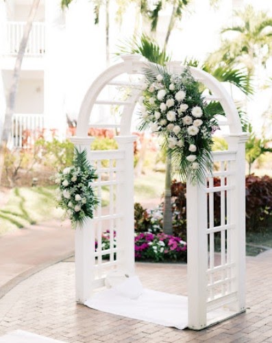 White garden arbor with white floral arrangements, surrounded by palms