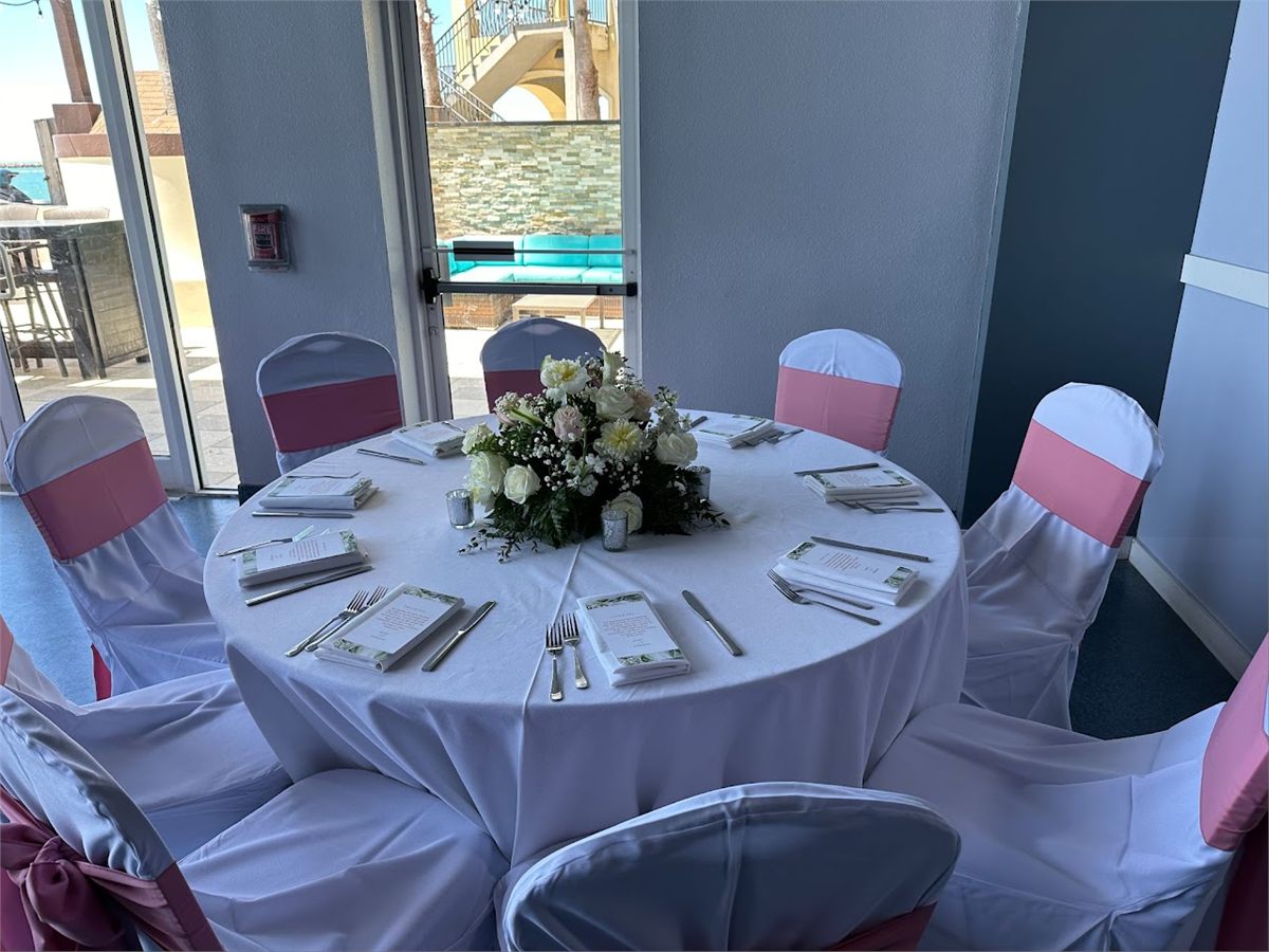 Round reception table with white linens, pink chair sashes and a white centerpiece