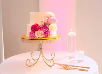 Two-tier white wedding cake decorated with pink and cream flowers on a gold stand