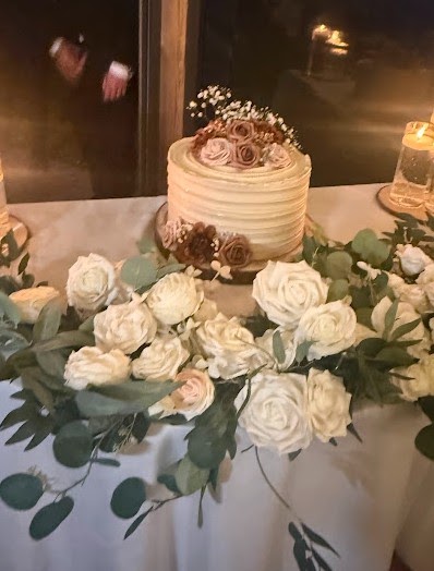 Single-tier cake beside a garland of cream and blush roses with eucalyptus along the table