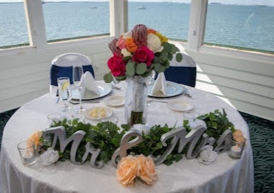 Sweetheart table with Mr and Mrs lettering and a bright mixed centerpiece beside a window over the water