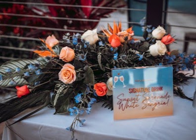 Orange and blue arrangements with tropical foliage beside a signature drink sign