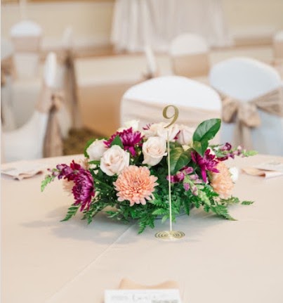 Low centerpiece of plum, peach and cream flowers beside a gold table number