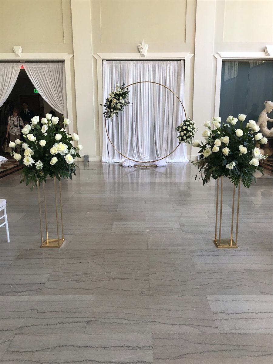 Circular floral arch with white draping, flanked by tall white rose arrangements on gold stands