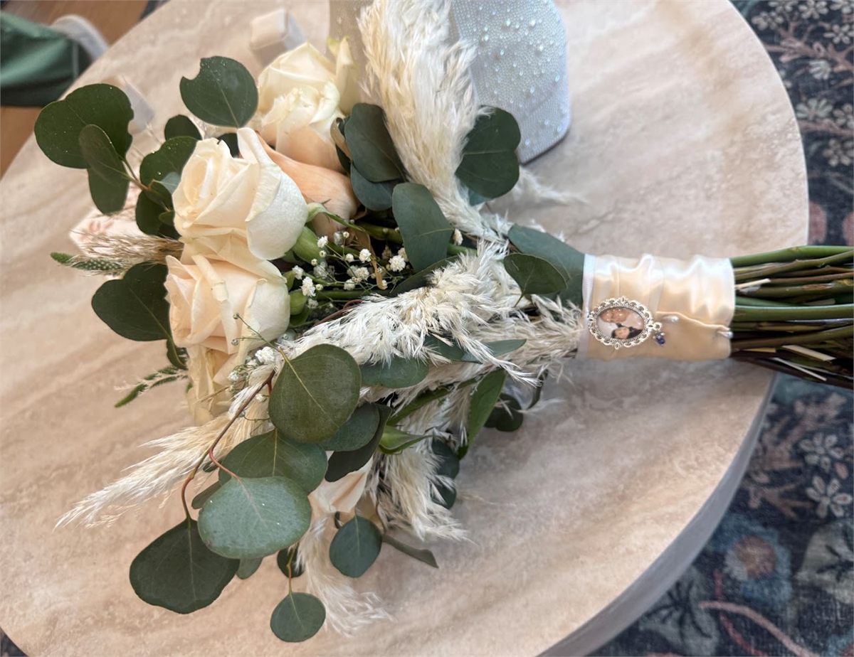Bridal bouquet of cream roses, eucalyptus and dried pampas grass resting on a wooden table