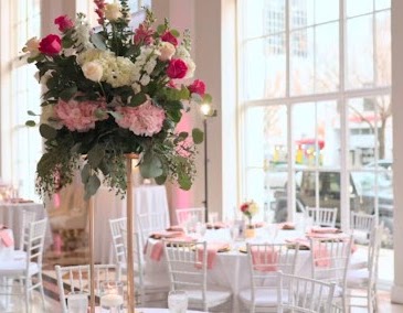 Tall pink and white centerpiece on a reception table in a bright room lined with windows