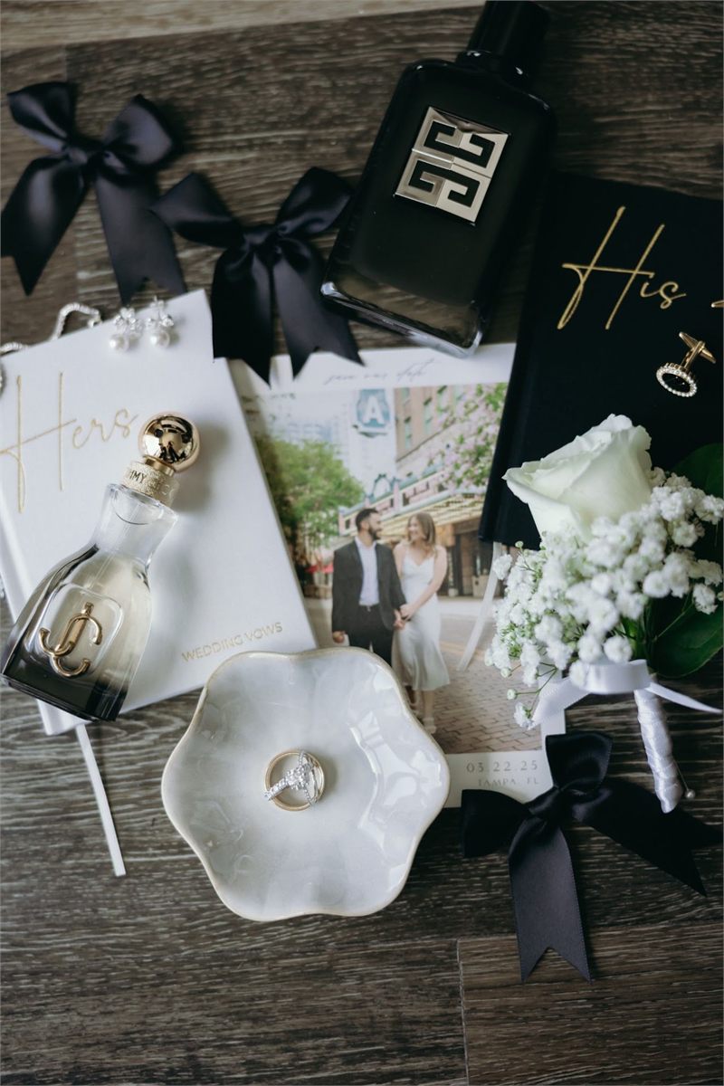 Wedding day details including rings and a boutonniere of white flowers tied with black ribbon