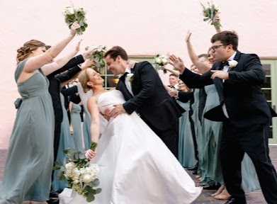 Wedding party cheering with bouquets raised as the groom dips the bride