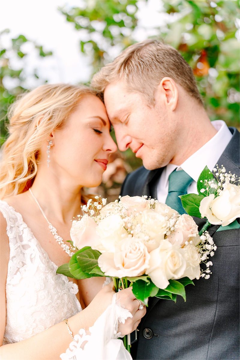 Bride and groom forehead to forehead, the bride holding a bouquet of white roses