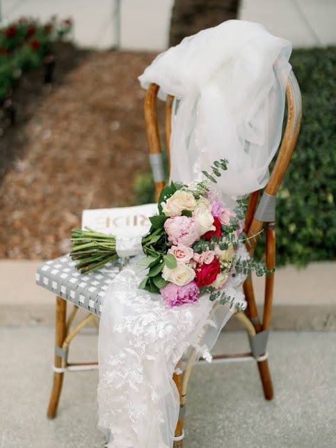 Bouquet of pink and cream flowers resting on a wooden chair with a veil
