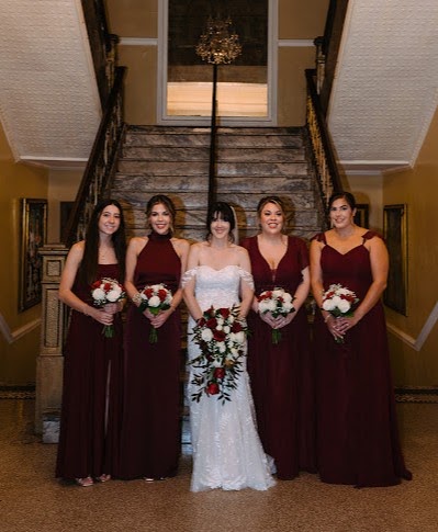 Bride and four bridesmaids in burgundy gowns holding red and white bouquets on a staircase