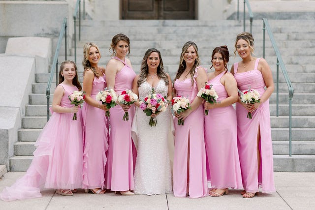 Bride and six bridesmaids in pink gowns holding pink and white bouquets on stone steps