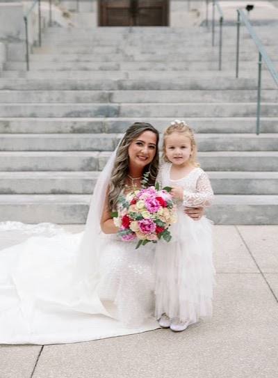 Bride kneeling beside a flower girl, holding a bright pink and white bouquet