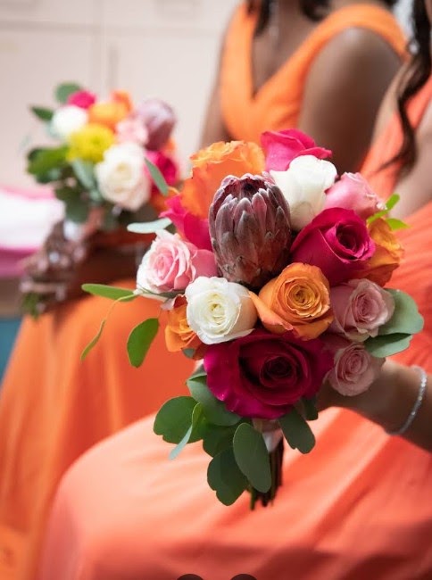 Bouquet of pink and orange roses with a protea, held by a bridesmaid in an orange dress