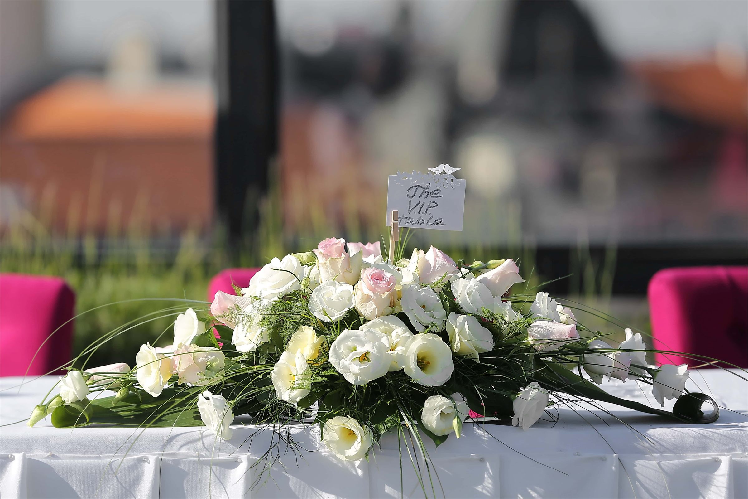 Long low arrangement of white roses and greenery running along the front of a head table